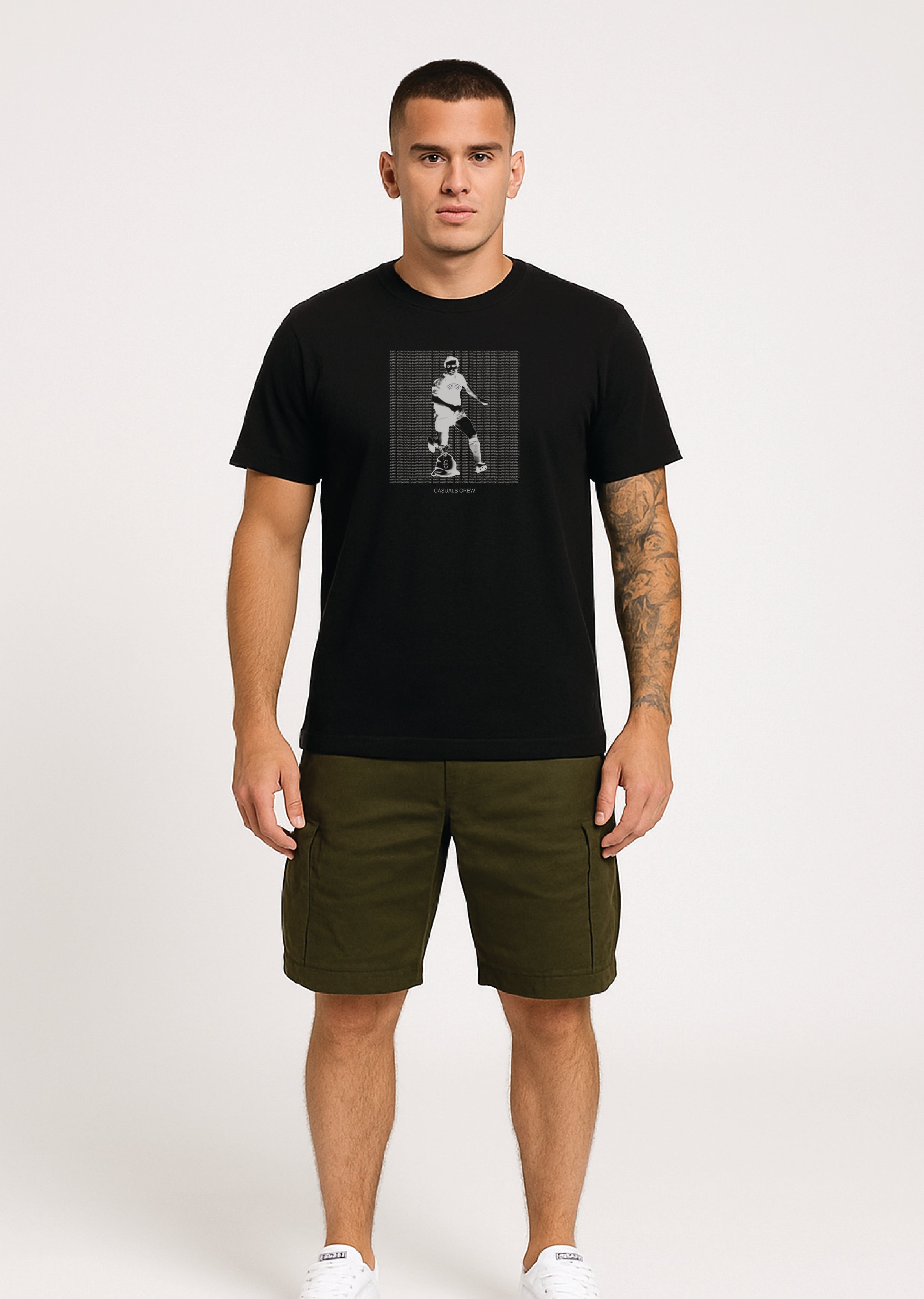 Man wearing a ultras black t-shirt with a against modern football graphic design and green shorts on a white background