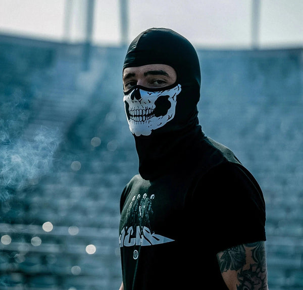Person wearing a black balaclava with a skull design in an outdoor setting