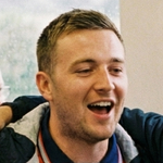 People sitting on a train, some wearing England football shirts, with a window view of greenery outside.