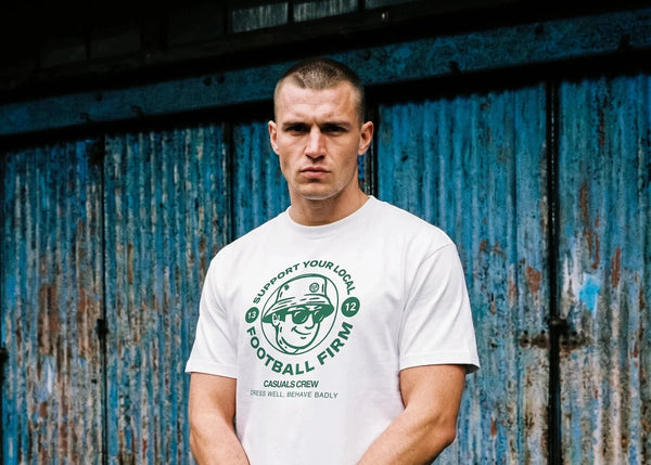 Man wearing a white t-shirt with a logo in front of a blue and rusted metal door.